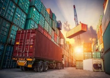 semi truck with stacks of shipping containers in port