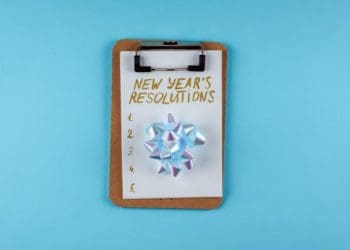 clipboard with silver bow and new year's resolutions list on blue background