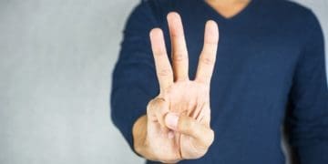 hand showing three fingers on gray background