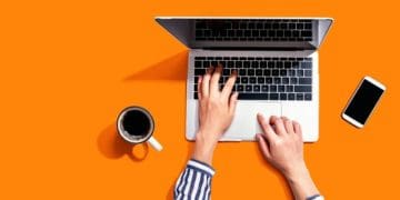 woman at laptop with coffee on orange background