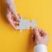 hands fitting puzzle pieces together on yellow background