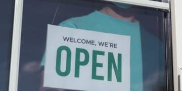 man flipping store sign to "welcome, we're open"