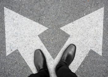 businessman in black shoes standing at the crossroad making decision which way to go