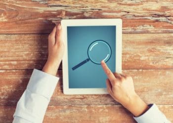 close up of male hands with magnifying glass picture on tablet pc
