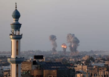 Explosions from Israeli rockets fired into Gaza are seen on the horizon past a mosque minaret.