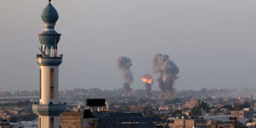 Explosions from Israeli rockets fired into Gaza are seen on the horizon past a mosque minaret.