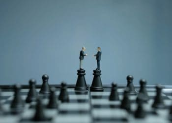 small businessmen figures shaking hands atop two chess pieces