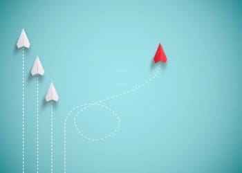 red paper plane out of line with white paper planes, concept of disruption