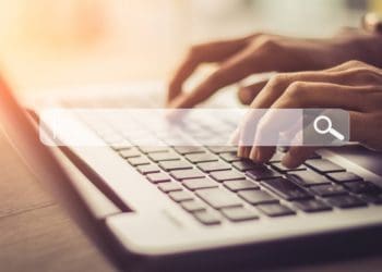 hands typing on laptop with search bar overlay