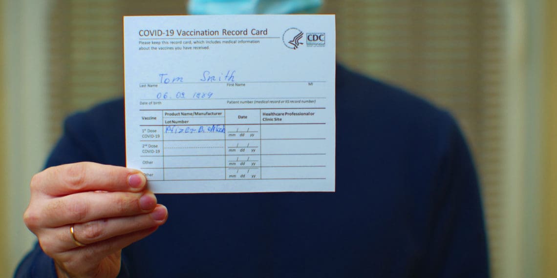 A masked professional holds up their covid-19 vaccination card.