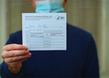 A masked professional holds up their covid-19 vaccination card.