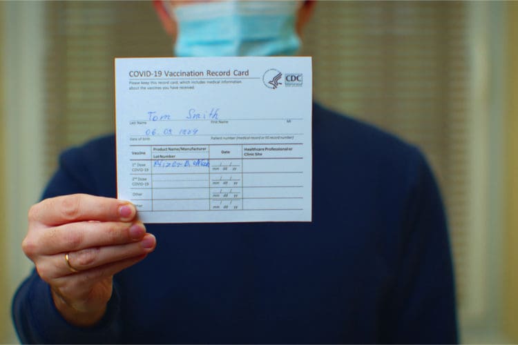 A masked professional holds up their covid-19 vaccination card.