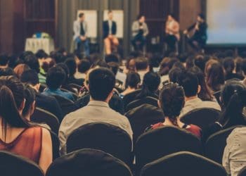 room of conference attendees with multiple speakers on stage