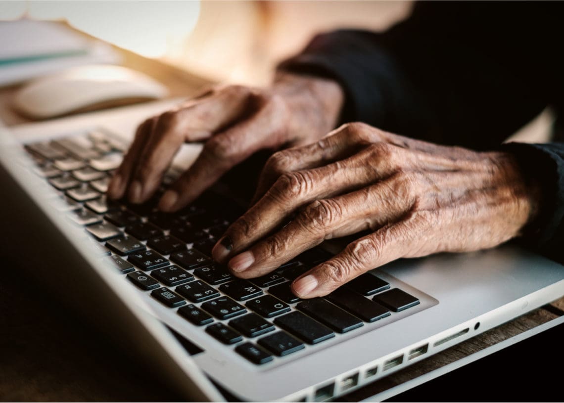 Old hands type on a laptop keyboard
