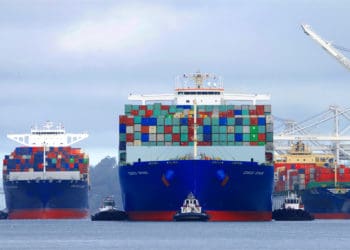 Three cargo ships loaded with containers sit in a port