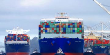 Three cargo ships loaded with containers sit in a port