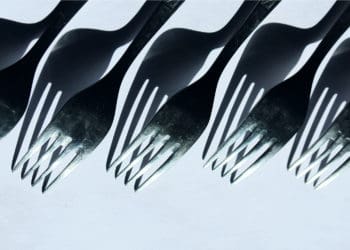 A row of forks and there shadows appear before a white background.