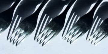 A row of forks and there shadows appear before a white background.