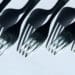 A row of forks and there shadows appear before a white background.