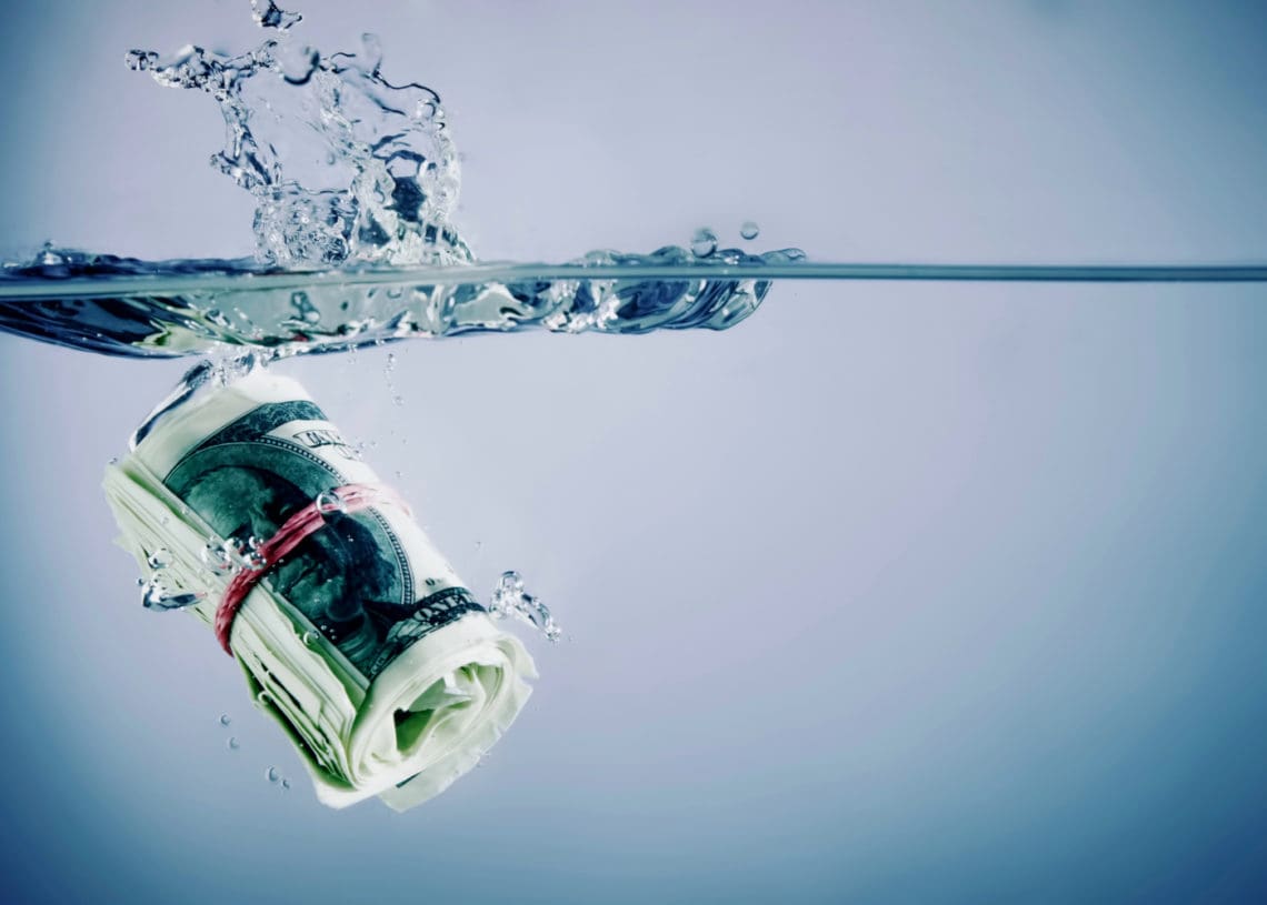 A roll of cash sinks in water.