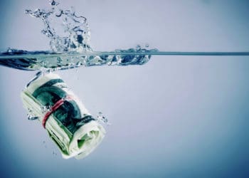 A roll of cash sinks in water.
