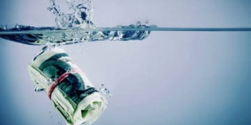 A roll of cash sinks in water.