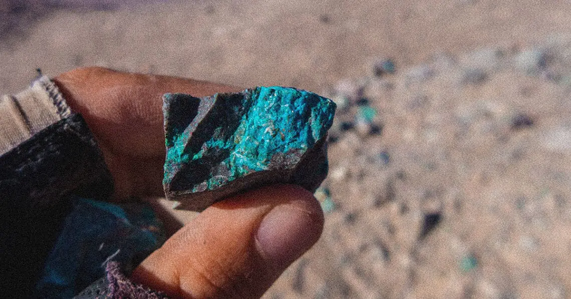 Fingers hold a rock with blue veins of a mineral