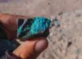 Fingers hold a rock with blue veins of a mineral