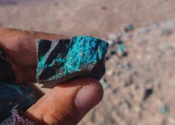 Fingers hold a rock with blue veins of a mineral
