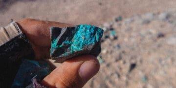 Fingers hold a rock with blue veins of a mineral
