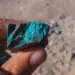 Fingers hold a rock with blue veins of a mineral